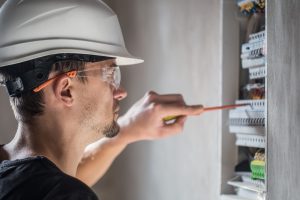 Man, an electrical technician working in a switchboard with fuses. Installation and connection of electrical equipment. Professional with tools in hand. concept of complex work, space for text.